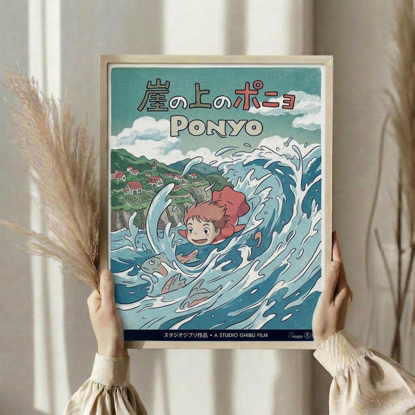 May include: Hands holding framed Studio Ghibli Ponyo poster in light wooden frame against white curtained window. Artwork shows red-haired Ponyo character swimming in swirling blue ocean waves with small coastal village and green hills in background. Japanese text at top, teal and blue color scheme. Dried pampas grass visible on left side.