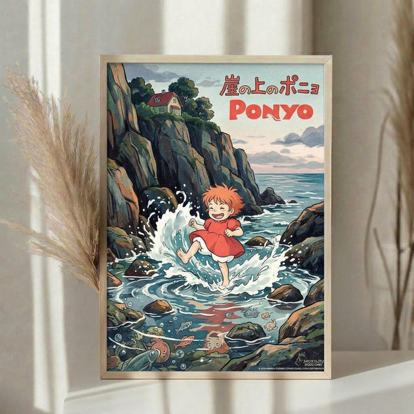 May include: Framed Studio Ghibli Ponyo poster displayed on light wooden surface with dried pampas grass beside it. Shows red-haired child character splashing in ocean waves surrounded by rocky coastal cliffs, house perched on clifftop, and sea creatures underwater. Vintage-style illustration with soft blues, greens, and coral tones in thin gold frame against neutral curtained background.