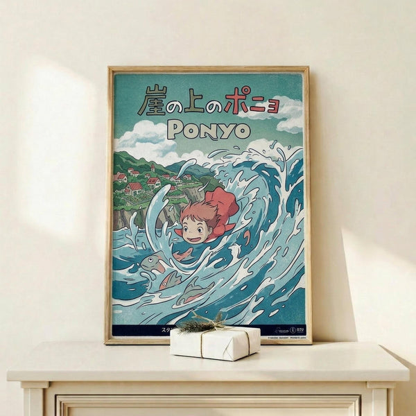 May include: Framed Studio Ghibli Ponyo poster displayed on light wood shelf against white wall. The colorful anime-style artwork shows red-haired Ponyo character swimming through dynamic blue ocean waves with a fish, green hillside village visible in background under cloudy sky. Japanese text at top with "PONYO" in white letters below. Small white wrapped gift with dried plant sprig sits beside the thin wooden frame.