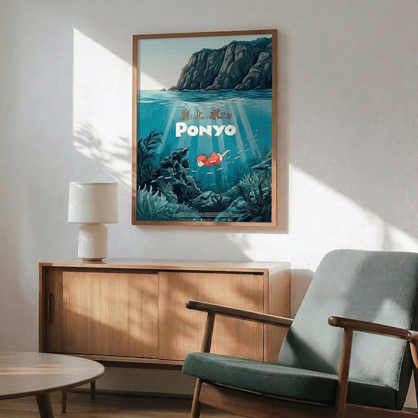 May include: Framed Ponyo movie poster displayed above mid-century modern wooden credenza in minimalist living room. Poster shows underwater scene with character swimming near rocky coastline in blue-green tones. Gray upholstered chair with wooden arms and small white table lamp visible. Natural sunlight casts geometric shadows on white wall.