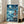 May include: Framed poster featuring animated young girl in red dress standing on rocky cliff overlooking turbulent blue ocean under crescent moon and swirling night sky. Japanese text at top with English subtitle. Poster displayed in bright living room with beige sofa, white walls, and natural lighting from windows.