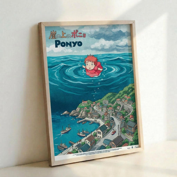 A framed poster featuring Studio Ghibli's Ponyo artwork in a light wood frame, leaning against a white wall. The illustration shows the red-haired character Ponyo floating in blue ocean water with bubbles around her, above a detailed coastal village with small houses, boats in a harbor, and green hillsides. Japanese text appears at the top along with "PONYO" in blue letters. The artwork has vibrant blues, greens, and warm earth tones in classic anime animation style.