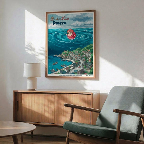 May include: Framed Studio Ghibli Ponyo poster displayed on white wall above wooden sideboard with lamp. Shows red-haired Ponyo character swimming in ocean waves above coastal Japanese town. Mid-century modern living room setting with teal armchair, round coffee table, and natural lighting creating geometric shadows on wall.