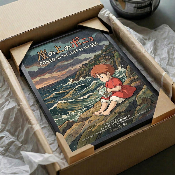 May include: Framed Ponyo on the Cliff by the Sea poster print in wooden frame, packed in cardboard box with tissue paper wrapping. Artwork shows red-haired Ponyo character sitting on rocky coastline reading, with ocean waves and cliffs in background. Vintage-style illustration with muted greens, blues, and earth tones. Japanese and English text visible at top. Frame appears medium-sized, nestled in protective packaging materials.