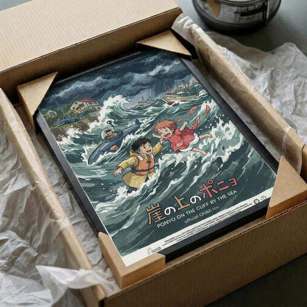 May include: Framed Studio Ghibli Ponyo movie poster in cardboard shipping box with protective wrapping. Artwork shows animated characters including red-haired girl and boy in yellow jacket amid stormy ocean waves with fishing boats and coastal buildings. Japanese text at bottom. Dark frame against white tissue paper packaging.