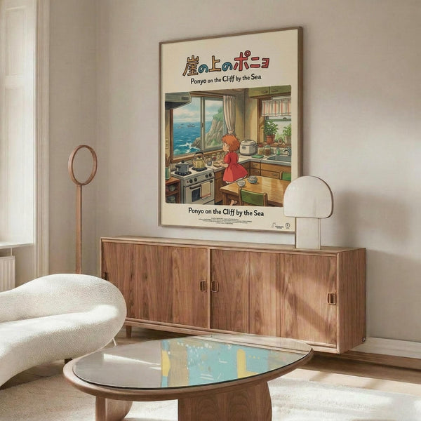May include: Framed Studio Ghibli Ponyo poster mounted above wooden mid-century modern credenza in minimalist living room. Poster shows red-haired child character cooking in cozy kitchen overlooking ocean cliffs. Room features cream upholstered chair, glass-top oval coffee table, white table lamp, and warm natural lighting creating shadows on light walls.