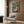 May include: Studio Ghibli Ponyo on the Cliff by the Sea movie poster mockup displayed in modern living room with beige armchair, geometric pillow, gold floor lamp, and dark wood wall panels. Poster shows red-haired child character sitting on rocky coastline with Japanese text at top.