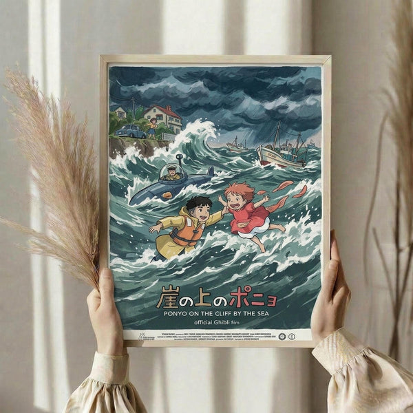 May include: Person holding framed Studio Ghibli Ponyo movie poster in natural light by window. Animated scene shows two children in stormy ocean waves with submarine and boats. Dramatic blue-green seascape with white foam, dark storm clouds above coastal houses. Japanese and English text at bottom. Light wood frame, pampas grass visible to left side.