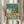 May include: Hands holding a framed Studio Ghibli-style poster featuring children and characters swimming in turquoise ocean waves near a clifftop house. The vintage-inspired artwork shows fish swimming below while fluffy white clouds fill the sky above. Japanese text appears at the top with "Ponyo" in English below. The poster has a natural wood frame and is photographed against white curtains with dried pampas grass visible on the left side.