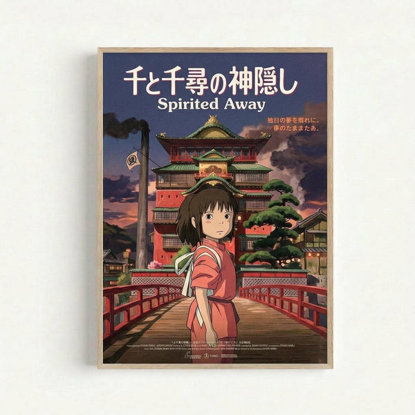 Framed movie poster featuring an anime girl in a red kimono standing on a wooden bridge. Behind her is a large traditional Japanese bathhouse with multiple stories, green roofs, and glowing windows set against a purple twilight sky. The poster has Japanese text at the top with "Spirited Away" in English below. The artwork is displayed in a light wooden frame against a white background.