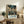 May include: Framed Spirited Away movie poster in light wood frame displayed on rustic wooden sideboard next to fern plant, cream throw pillow, and ceramic vases. Poster shows anime girl character in bustling Japanese street market scene with lanterns and traditional architecture in teal and warm tones.