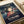 May include: Spirited Away movie poster featuring Chihiro, a young girl with brown hair in red clothing, surrounded by small white spirits against a twilight landscape with a train track. The poster displays both English and Japanese text at top and bottom. Shown as a print on white paper placed on a beige couch or cushioned surface.