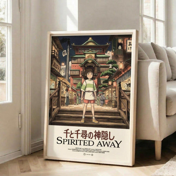 May include: Framed Spirited Away movie poster leaning against white wall next to beige sofa in bright living room. Poster shows young girl in green and white outfit standing on wooden bridge facing ornate Japanese bathhouse with colorful lanterns and traditional architecture. Artwork features rich detail in anime style with warm lighting. Japanese and English text below illustration. Light wood frame, approximately 2-3 feet tall based on furniture scale.