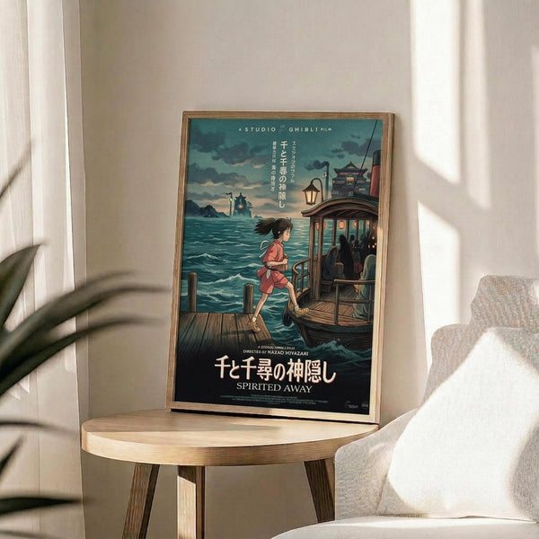 May include: Framed Studio Ghibli Spirited Away movie poster displayed on round wooden side table next to beige upholstered chair. Poster shows young girl in red outfit stepping from wooden dock onto traditional boat, with ocean and mystical buildings in background. Natural lighting creates soft shadows across white wall and plant leaves visible in corner.