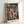 May include: Framed Spirited Away movie poster featuring main character Chihiro in traditional red outfit standing before fantastical Japanese architecture with pagodas, bridges, and spirit world buildings. Poster displays Japanese and English text including "Studio Ghibli Present" at top. Light wood frame sits against white wall with soft lighting creating gentle shadows.