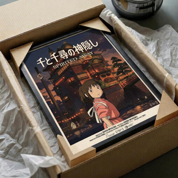 May include: Framed Spirited Away movie poster featuring young Chihiro in red striped outfit against twilight bathhouse backdrop, packed in cardboard shipping box with protective padding and wooden frame corners visible