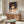 May include: Framed anime poster featuring young girl with dark hair surrounded by white spirits, displayed above wooden sideboard in modern living room with white upholstered chair, glass coffee table, and neutral walls with natural lighting
