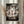 May include: Framed Studio Ghibli Spirited Away movie poster hanging on cream wall next to dried pampas grass. Poster shows young girl Chihiro standing under traditional Japanese torii gate surrounded by colorful spirit characters including No-Face, dragon Haku, and soot sprites. Artwork features muted greens, pinks and earth tones with Japanese and English text at bottom in decorative black border.