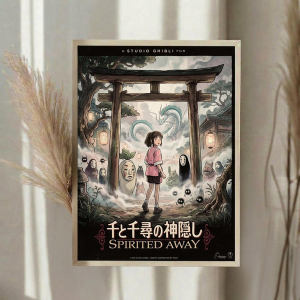 May include: Framed Studio Ghibli Spirited Away movie poster hanging on cream wall next to dried pampas grass. Poster shows young girl Chihiro standing under traditional Japanese torii gate surrounded by colorful spirit characters including No-Face, dragon Haku, and soot sprites. Artwork features muted greens, pinks and earth tones with Japanese and English text at bottom in decorative black border.