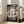 May include: Framed Studio Ghibli Spirited Away movie poster in light wood frame, leaning against white wall next to beige upholstered chair. Poster features young girl in pink shirt surrounded by Japanese torii gate, dragon, No-Face character, and other mystical spirits in muted greens and earth tones. Sunlight streams through windows onto hardwood floor in bright, minimalist living room setting.