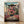 May include: Framed anime poster showing young girl in pink kimono leaping across red bridge with traditional Japanese bathhouse building behind her, mounted in light wood frame against white textured wall on wooden floor with soft natural lighting