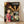 May include: Framed poster of animated film artwork featuring young girl in red kimono in foreground with various colorful spirit characters behind her in lantern-lit traditional Japanese street scene. Wooden frame sits on light wood floor against white wall with natural lighting creating soft shadows.