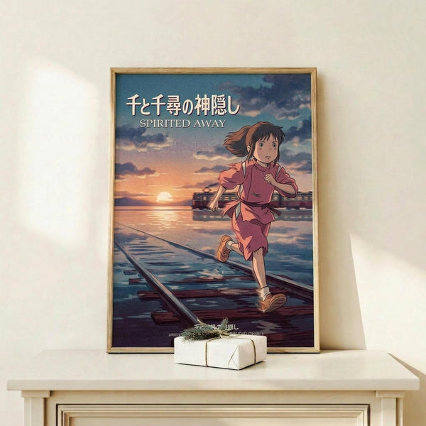 May include: Framed Spirited Away movie poster showing animated girl with brown hair in pink outfit running across flooded train tracks at sunset, displayed on light wood shelf next to small white wrapped gift with greenery, against cream wall in minimalist room setting