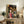 May include: Framed Spirited Away movie poster featuring Chihiro in red outfit with various animated characters in traditional Japanese street scene with paper lanterns, displayed on rustic wooden sideboard alongside books, ceramic vase, and fern plant in cozy living room setting with beige armchair and neutral walls.