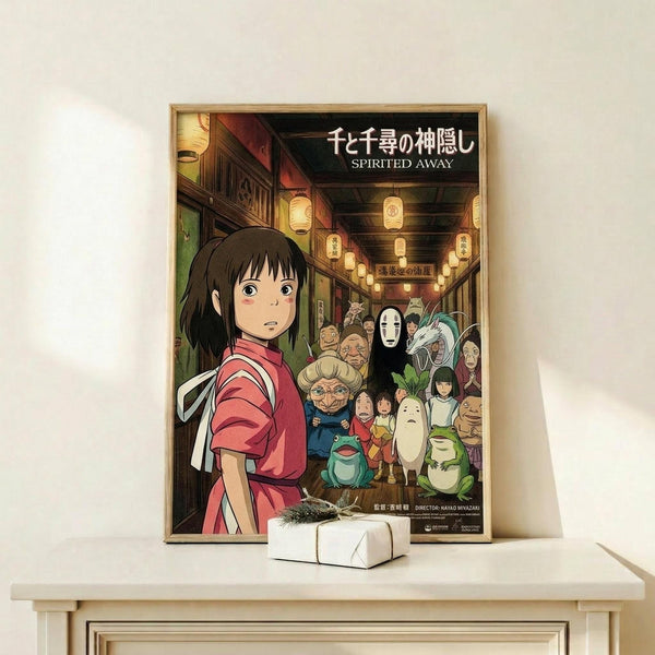 May include: Framed Spirited Away movie poster displayed on light wood shelf next to small white wrapped gift. Poster features young girl in red outfit surrounded by colorful animated characters in traditional Japanese street scene with paper lanterns. Artwork has vibrant colors with Japanese and English text at top. Natural lighting on white wall background.