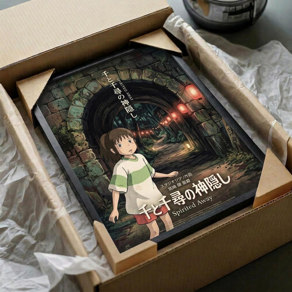 May include: Spirited Away movie poster in cardboard shipping box with protective wrapping, showing Chihiro character in green and white outfit standing in mystical stone tunnel with glowing red lanterns, surrounded by packing materials on white surface