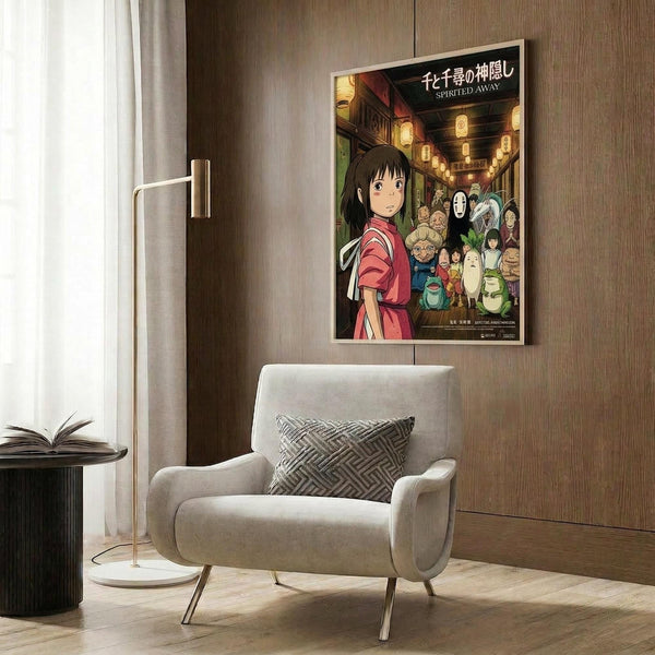 May include: Framed Spirited Away movie poster mounted on wood-paneled wall above modern beige armchair with geometric pillow. Poster shows young girl in pink kimono surrounded by animated characters including No-Face and colorful spirits. Contemporary living room setting with brass floor lamp, dark round side table with open book, and neutral tones throughout.