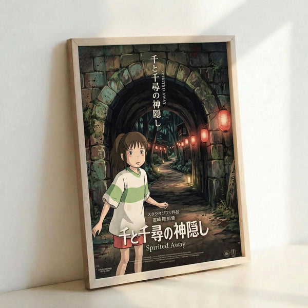 May include: Framed movie poster featuring animated young girl with brown hair in green and white striped shirt standing in stone archway tunnel with red lanterns glowing in background. Poster shows Japanese text and "Spirited Away" title, displayed in light wood frame leaning against white wall corner.