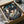 May include: Framed poster artwork featuring Chihiro from Spirited Away surrounded by white soot sprites in a magical bathhouse setting with traditional Japanese architecture, red lanterns, and intricate details. The poster sits in a cardboard shipping box with protective wrapping paper, photographed on a white surface next to a dark glass bowl.