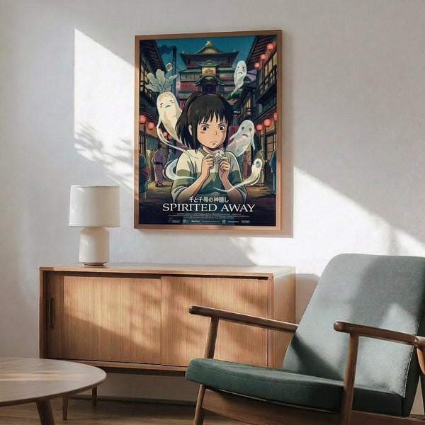 May include: Framed Spirited Away movie poster hanging on white wall above wooden sideboard with table lamp. Features anime girl with dark hair surrounded by white spirits and traditional Japanese bathhouse architecture in background. Mid-century modern living room setting with teal upholstered chair and round coffee table. Natural sunlight creates geometric shadows on wall. Poster shows vibrant blues and earth tones in detailed illustration style.