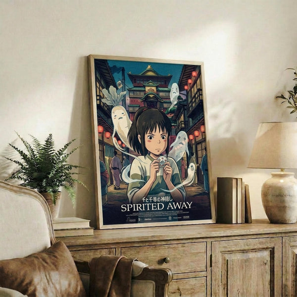 May include: Framed Studio Ghibli Spirited Away movie poster displayed on rustic wooden sideboard in cozy living room setting. Poster features young girl character surrounded by white spirits and traditional Japanese architecture with red lanterns. Natural wood frame, positioned next to fern plant, ceramic vase, and stacked books. Beige armchair visible in foreground.
