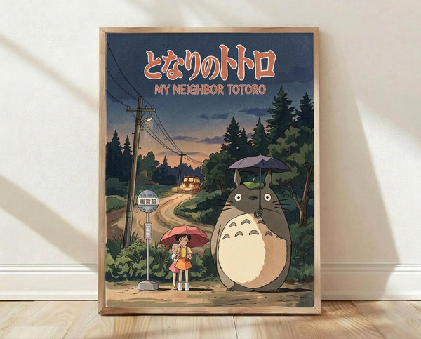 May include: Framed poster print showing iconic Studio Ghibli characters Totoro and a young girl with umbrellas standing at a rural bus stop. The artwork features a twilight scene with power lines, trees, and a distant bus, rendered in animated film style with muted blues, greens, and warm sunset tones. The wooden frame sits on light wood flooring against a white wall with natural lighting creating soft shadows.