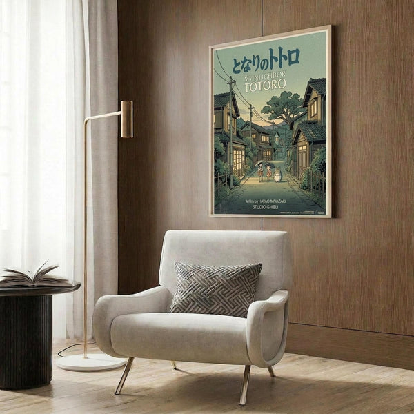 May include: Vintage-style My Neighbor Totoro movie poster mounted on wood-paneled wall above beige upholstered armchair. Poster features Japanese village scene with traditional houses, power lines, trees, and Totoro characters in muted green and brown tones. Modern reading nook setting with geometric pillow, brass floor lamp, and dark side table with open book.