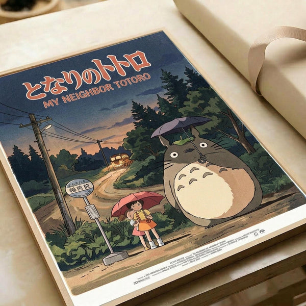 May include: Vintage-style anime poster print displayed on white paper with curved edges. Features iconic gray forest creature with white belly holding umbrella, standing near two children with red umbrella at rural bus stop. Scene shows twilight sky in blue and orange hues, green trees, telephone poles, and dirt road. Japanese text appears at top in red lettering against dusky background.