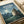 May include: Blue-toned movie poster featuring the beloved forest spirit character from Studio Ghibli's animated film, shown in a moonlit countryside scene with glowing fireflies, houses in the distance, and lush vegetation. The poster displays both English and Japanese text at the top and appears to be printed on cream-colored paper, photographed laying flat on white fabric with soft natural lighting.