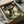 May include: Framed poster featuring Totoro characters in an enchanted forest scene with large tree, two children, and forest spirits in green and golden tones. Black frame shown in cardboard shipping box with protective wrapping materials on white surface.