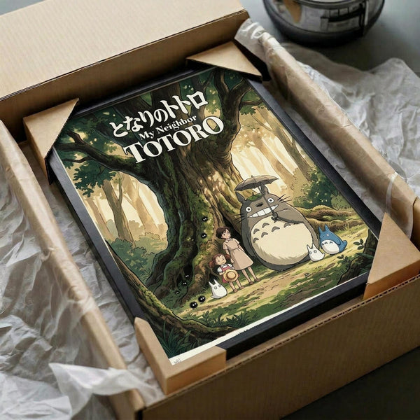 May include: Framed poster featuring Totoro characters in an enchanted forest scene with large tree, two children, and forest spirits in green and golden tones. Black frame shown in cardboard shipping box with protective wrapping materials on white surface.