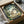 May include: Framed My Neighbor Totoro poster showing the iconic gray forest spirit with children in a lush green woodland scene, packaged in a cardboard box with protective wrapping paper. The vintage-style artwork features soft earth tones and detailed forest imagery, displayed as an unboxing scene on a neutral surface.
