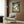 May include: Studio Ghibli My Neighbor Totoro movie poster mounted on wood-paneled wall above beige upholstered armchair with geometric patterned pillow. Poster shows large gray Totoro character with children and smaller forest spirits in green woodland setting. Modern reading nook with brass floor lamp and side table with open book.