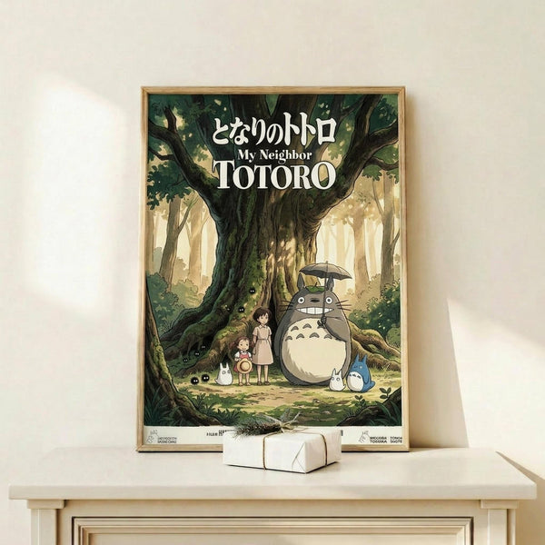 May include: Framed Studio Ghibli poster showing Totoro character with umbrella standing beside two children under a large tree in an enchanted forest. The artwork features soft greens and warm earth tones in classic anime illustration style. Wooden frame sits on light wooden shelf with small white decorative box against cream wall.