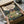 May include: Hands holding a framed vintage-style poster featuring the iconic forest spirit Totoro and two children in a magical woodland scene with a cozy house in the background. The artwork displays warm earth tones and Studio Ghibli's distinctive animation style. The black-framed print is being unpacked from brown cardboard packaging with white tissue paper on a light wooden surface.