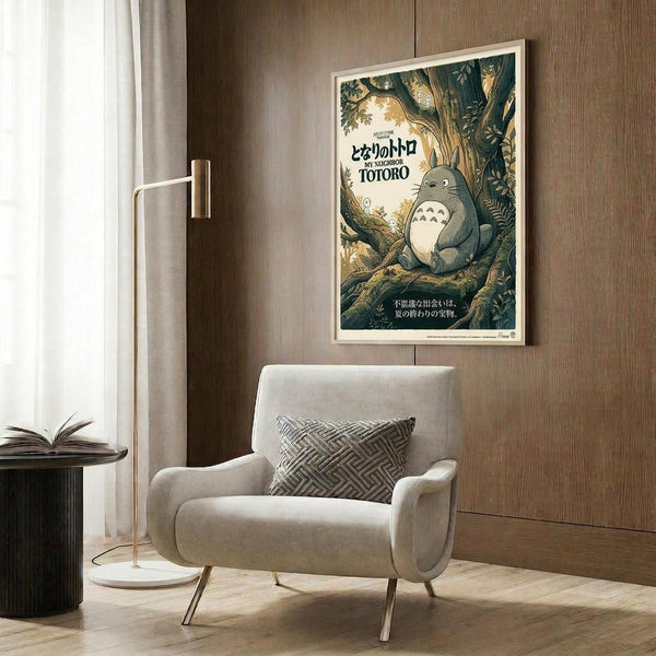 May include: Framed My Neighbor Totoro movie poster hanging on wood-paneled wall above beige upholstered armchair with geometric patterned pillow. Poster features gray Totoro character sitting in lush green forest with Japanese text. Modern reading nook with brass floor lamp, dark round side table with open book, and white curtains visible.