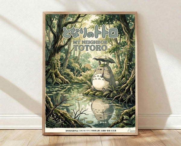 May include: Framed poster print featuring Totoro sitting by a forest pond holding an umbrella, with his reflection visible in the water. Japanese and English text at top reads "My Neighbor Totoro." Artwork shows lush green forest setting with detailed trees, ferns, and lily pads. Print displayed in light wood frame leaning against white wall on wooden floor with soft natural lighting and shadows.