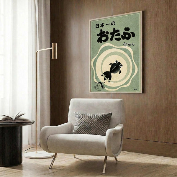 May include: Vintage-style Japanese poster with green background featuring black goldfish silhouette surrounded by concentric circles, displayed in light wood frame on wood paneled wall above beige upholstered chair with geometric patterned pillow, next to brass floor lamp and dark round side table with open book