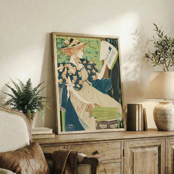 May include: Vintage Art Nouveau poster in light wood frame showing woman in green hat with flowers reading papers, displayed on rustic wooden sideboard with books, ceramic vases, and fern plants in neutral-toned living room setting