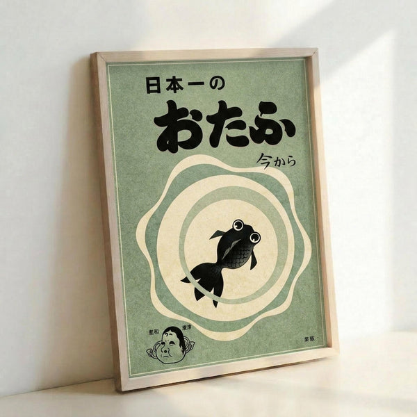 May include: Framed poster with sage green background featuring Japanese text at top, black silhouette of a goldfish with large round eyes in center surrounded by cream-colored concentric circles, small cartoon face illustration in bottom left corner, displayed in light wooden frame leaning against white wall